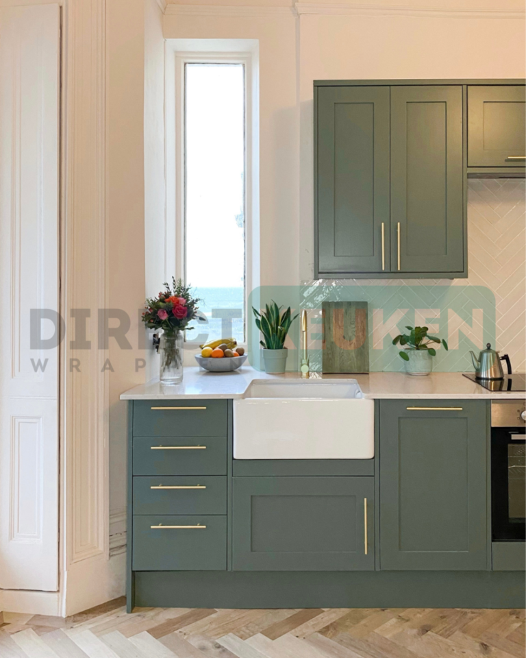 Groene keuken met kaderdeuren, messingkleurige grepen en een witte spoelbak